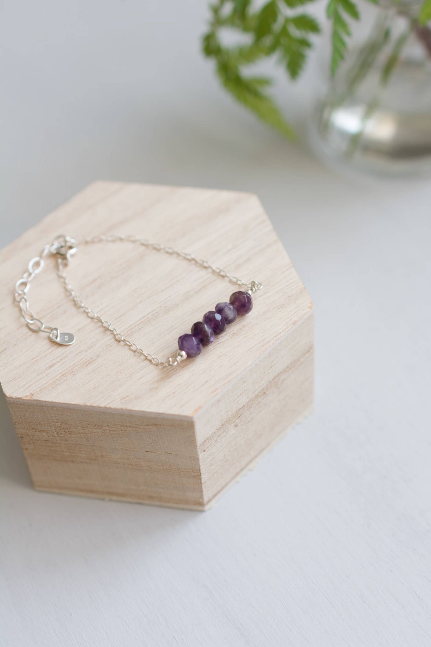 Amethyst bracelet on a wooden jewelry box with a plant in the background