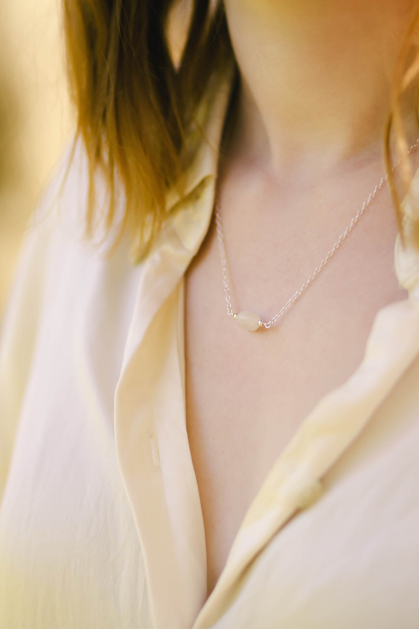 Necklace with a small pendant worn by a person in a light-colored shirt.
