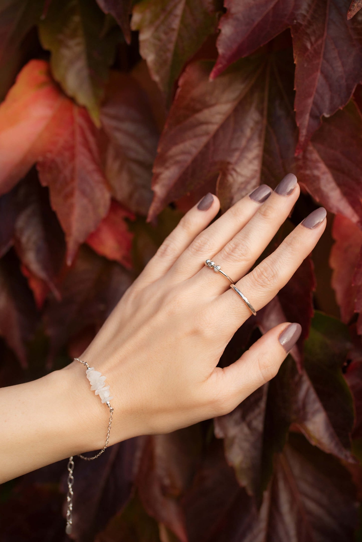 A woman's hand wearing two dainty sterling silver rings and a white moonstone bracelet on her wrist.