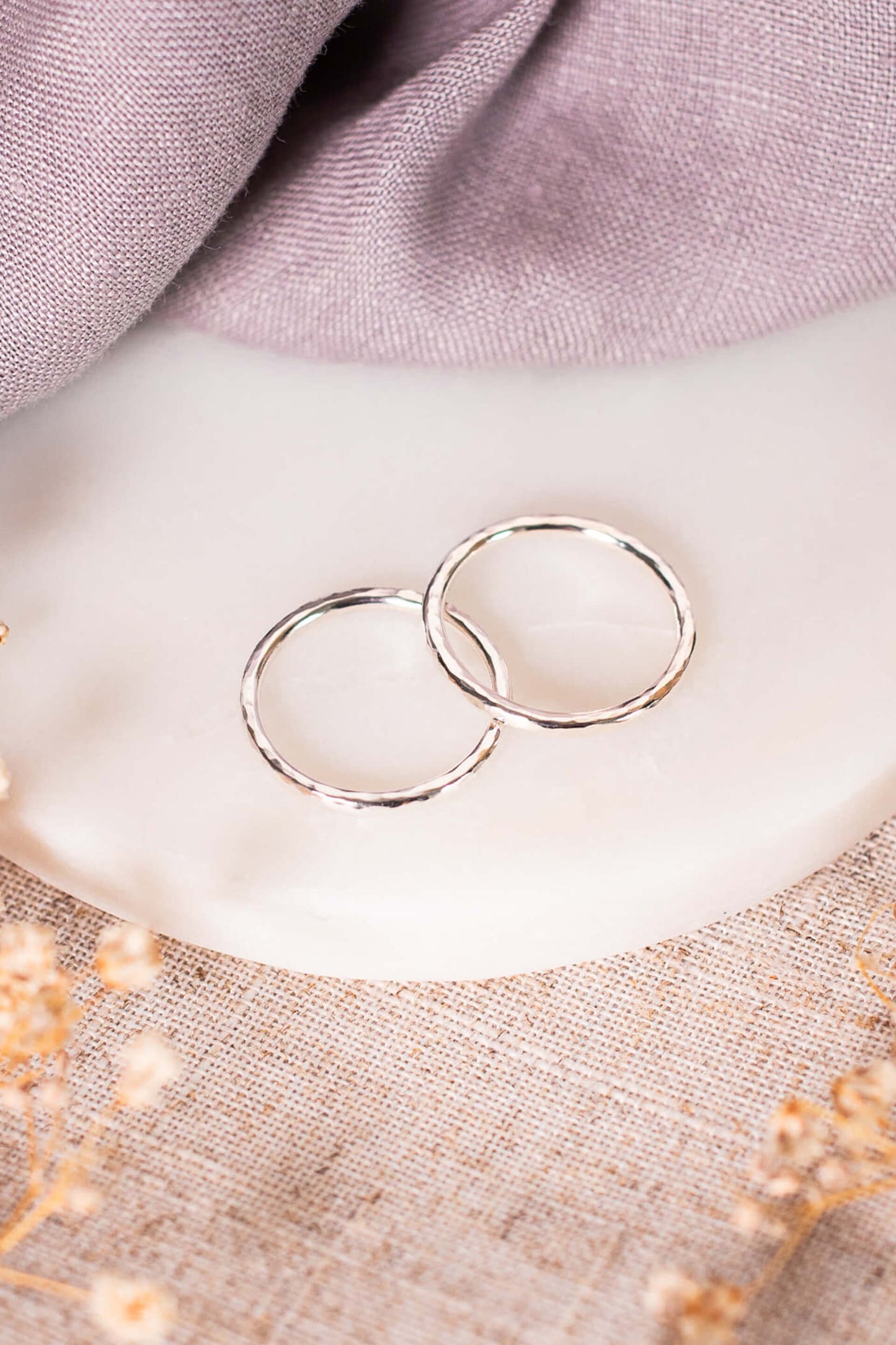 Two sterling silver rings lie overlapping on a piece of white marble.