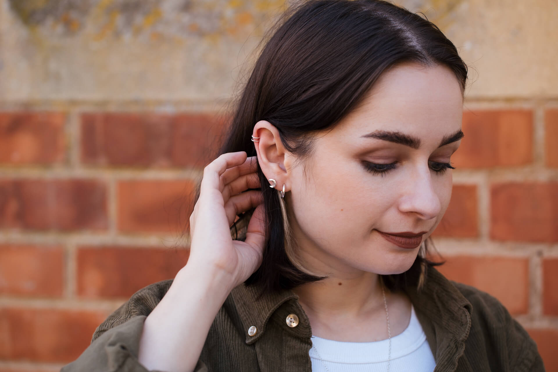 Woman adjusting an earring against a brick wall background