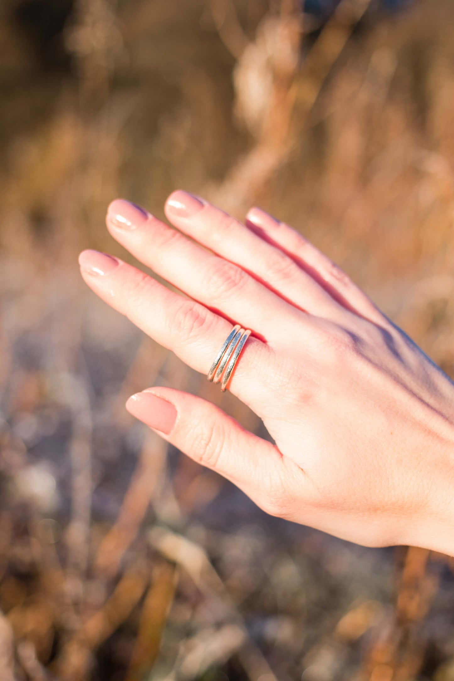 A woman's hand wearing a stack of three textured sterling silver rings on her index finger.