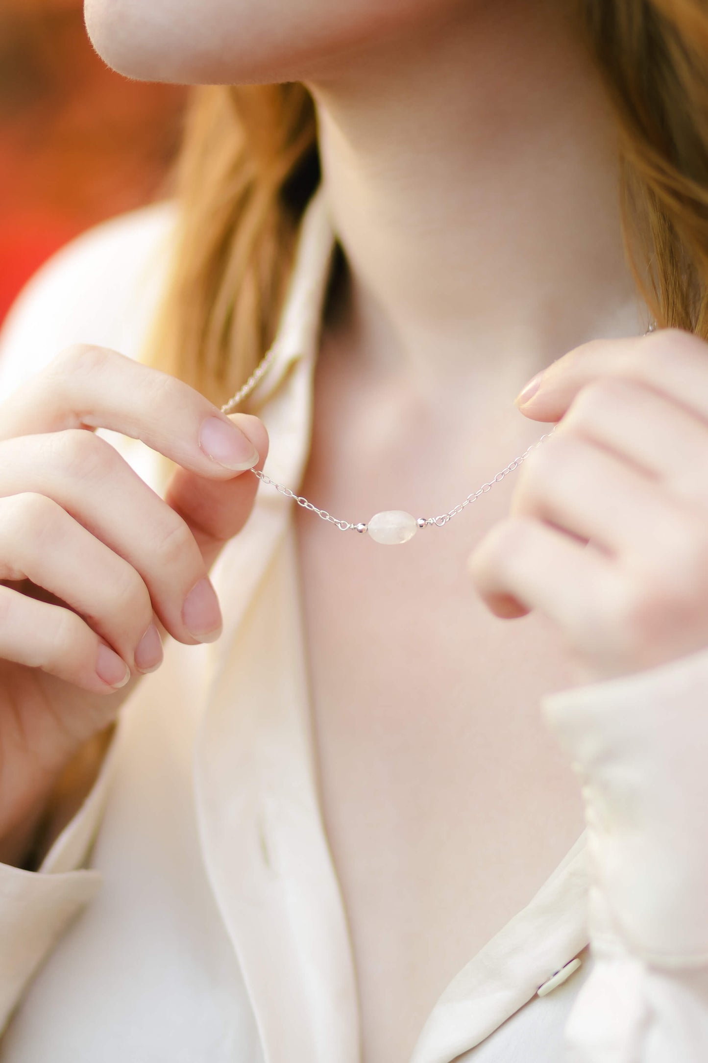 Close-up of a person wearing a delicate necklace with a moonstone pendant.