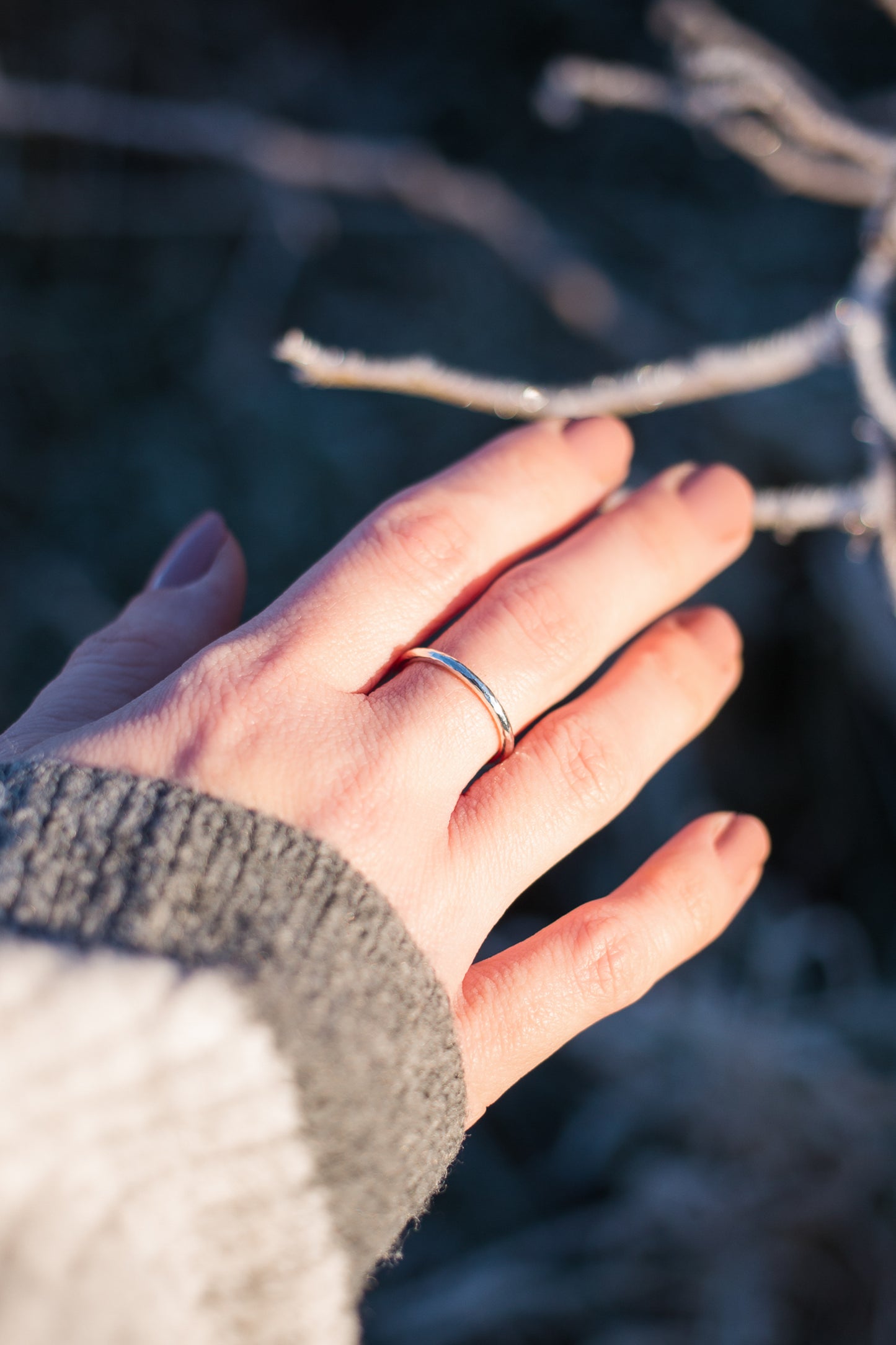 A woman's hand wearing a slim sterling silver ring band.