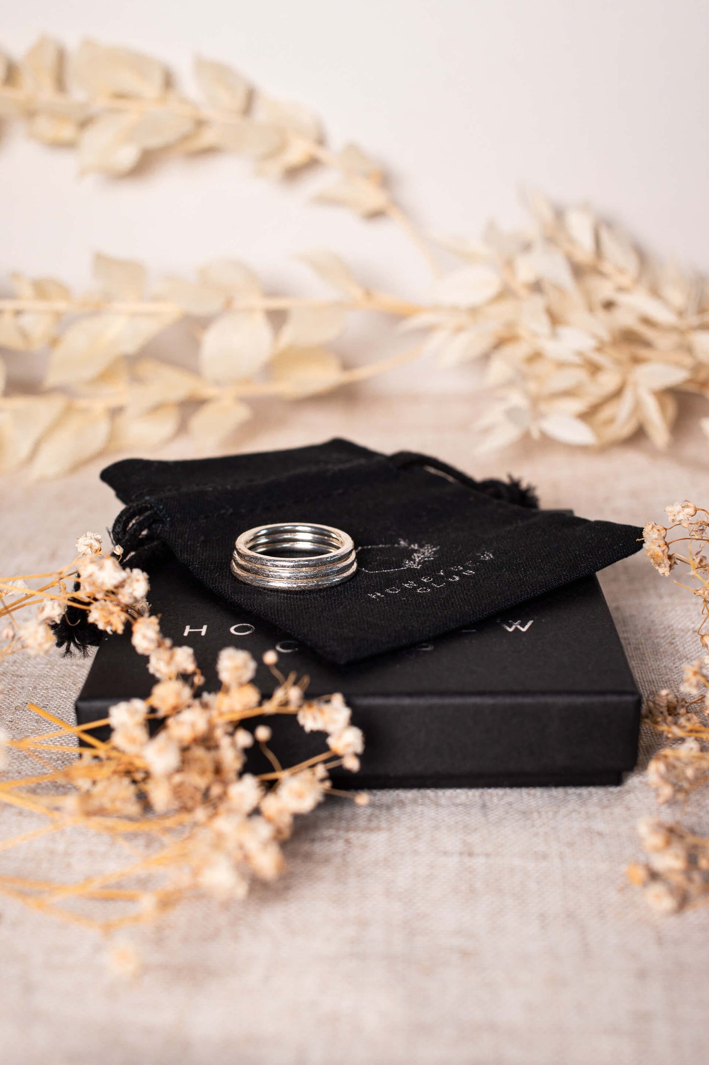 A stack of three textured sterling silver rings lie on black gift packaging.