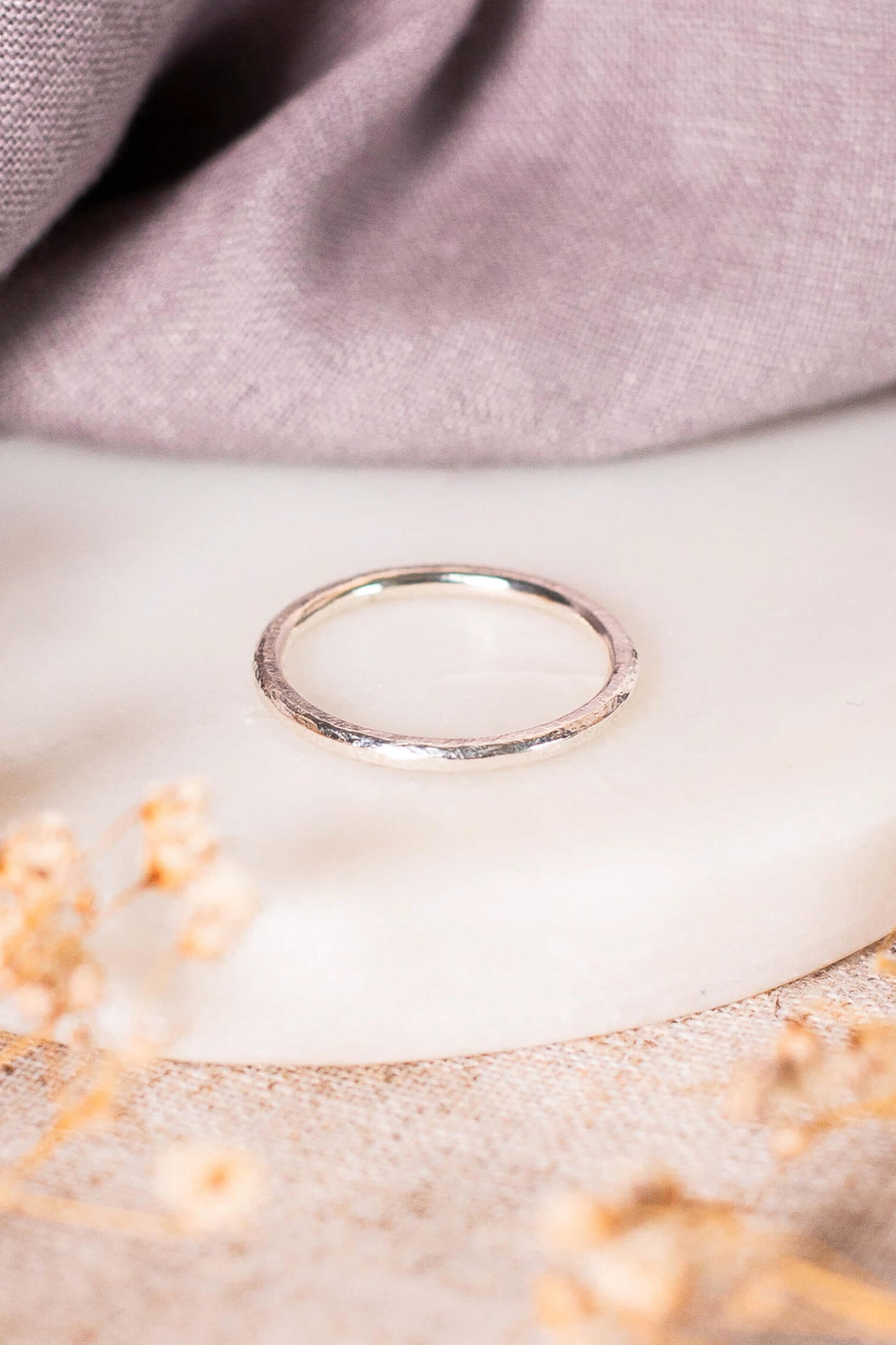 A sterling silver ring with a textured surface lies on a piece of round marble. The ring is smooth and shiny on the inside.
