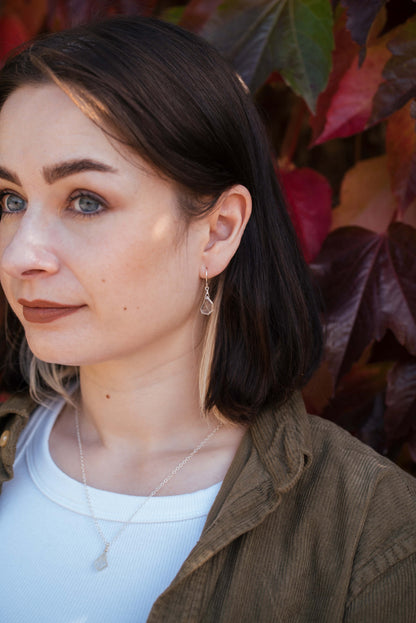 Young woman wearing small, clear gemstone earrings with a matching silver necklace