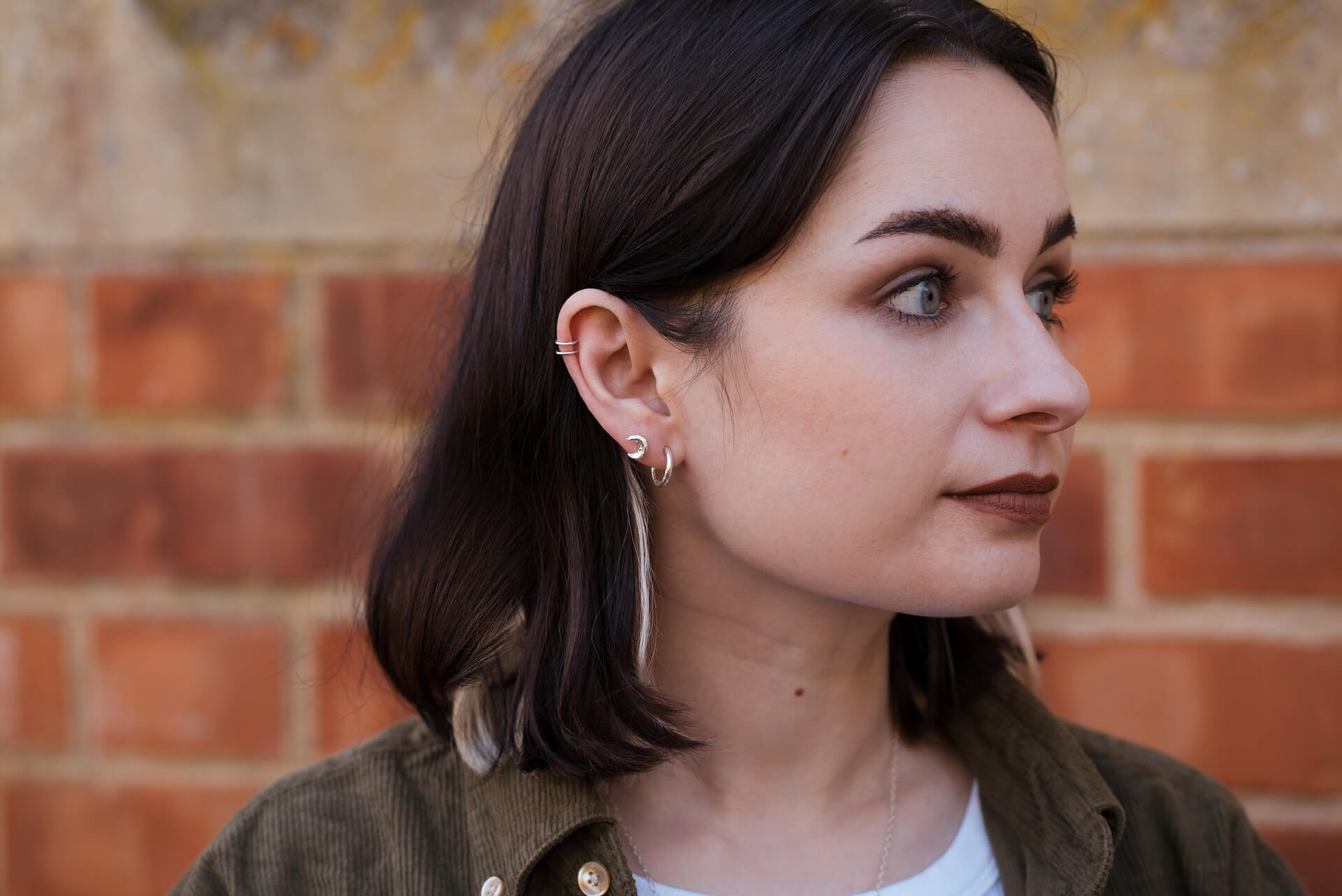 Young woman with dark hair wearing three sterling silver earrings.